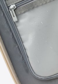 Zbliżenie na szarą saszetkę na zamek z przezroczystą, wodoodporną częścią, na której widoczne są krople wody.