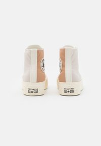 Wysokie trampki z beżową i białą cholewką z płótna, z okrągłą naszywką z logo, kremową podeszwą środkową i gumową podeszwą zewnętrzną.