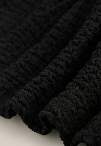 Tissu noir texturé avec un motif froissé, présentant des bords doux et fluides. Le matériau semble léger et légèrement transparent.