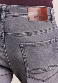 Szare dżinsy z denimu o fakturowanym wykończeniu, z brązową skórzaną naszywką z napisem "BOSS ORANGE" oraz dwoma tylnymi kieszeniami z detalami przeszyć.