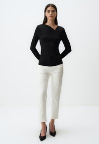Zwarte langemouwen top met een V-hals ontwerp, voorzien van gestructureerde stof en een getailleerd silhouet, gecombineerd met witte slim-fit jeans en zwarte hakken.