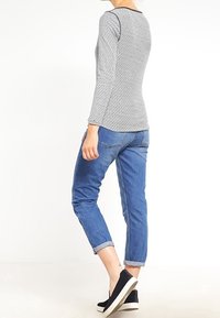 Gray long-sleeve top with a textured pattern, dark neckline, paired with rolled-cuff blue jeans and black slip-on shoes with white soles.