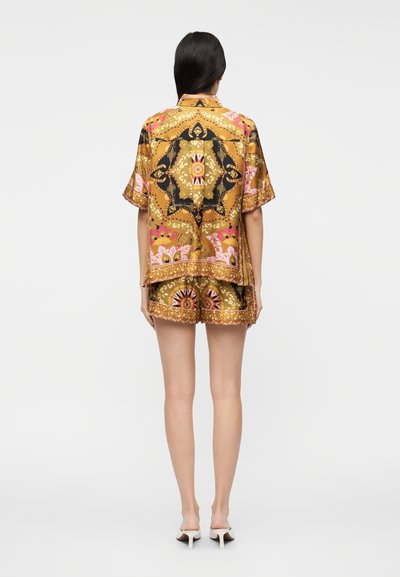 Short-sleeve, patterned shirt in gold, pink, and black; matching shorts with decorative hem. Smooth fabric, relaxed fit.