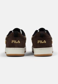 Bruna mockaskor med vita och gummisula. Gula detaljer nära hälen. "FILA"-logotyp i guld på baksidan. Låg toppdesign.