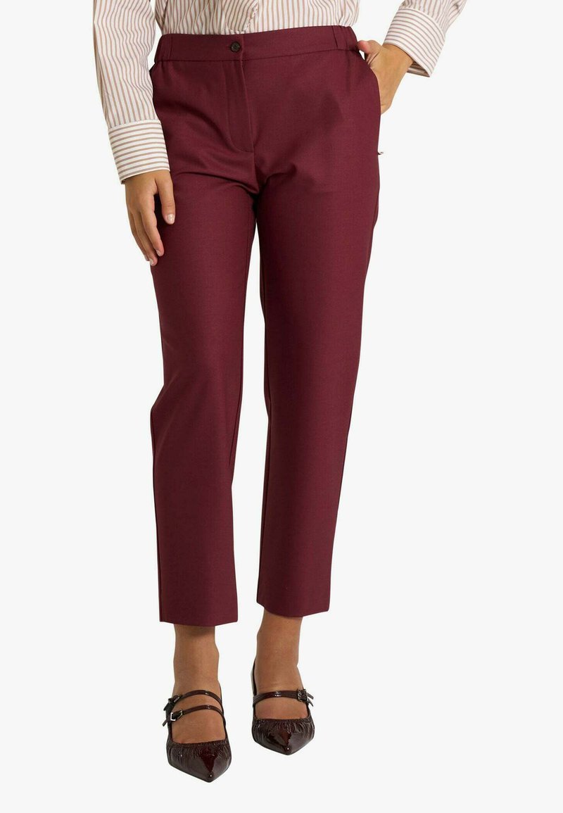 Pantaloni burgundy su misura con una consistenza liscia e una gamba dritta, caratterizzati da una chiusura frontale con bottoni e tasche laterali. Indossati con scarpe nere a punta.