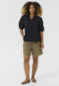 Blusa nera con bottoni e maniche a sbuffo, abbinata a pantaloni corti verde oliva con un sottile ricamo floreale. Ballerine con stampa animalier marrone.