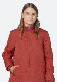 Chaqueta acolchada roja con cuello alto, cierre frontal y bolsillos laterales; el patrón de diamantes texturizado y los puños acanalados aumentan la calidez.