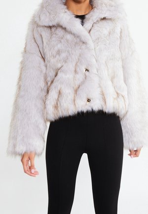 Veste courte en fausse fourrure blanche avec manches longues portée sur un pantalon noir taille haute ajusté, portée par une personne debout.