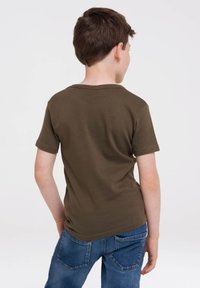 Camiseta de algodón de color verde oliva y manga corta, con cuello redondo y mangas enrolladas, combinada con unos jeans de mezclilla azul.