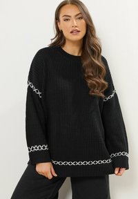 Maglione nero a maglia con una vestibilità ampia e maniche lunghe. Presenta accenti bianchi ricamati lungo le maniche e l'orlo. Tessuto strutturato.