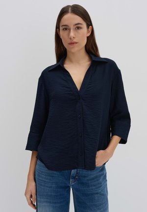 Navy blue, textured shirt with a collar, long sleeves, and buttons down the front, paired with blue denim jeans.