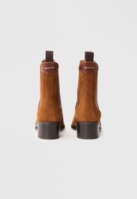 Br�ązowe zamszowe botki za kostkę z czarnym słupkowym obcasem, z akcentem ze skóry na górze z złotym brandingiem oraz elastycznymi panelami bocznymi ułatwiającymi zakładanie.