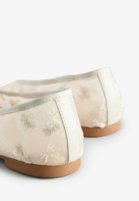 Lichtbeige ballet flats van gaasstof met geborduurde bloemenpatronen, een effen crème rand en een bruine rubberen zool.