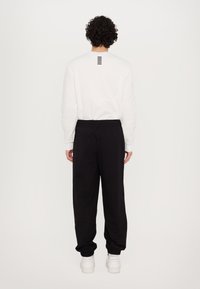 White sweatshirt featuring a black stripe detail on the back, paired with black sweatpants and white sneakers. Casual athletic wear.