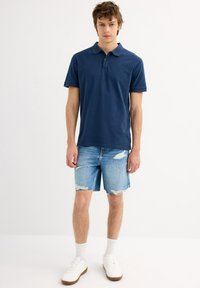Polo de marinero de manga corta, combinado con pantalones cortos de mezclilla azul claro con detalles desgastados. Usado con zapatillas blancas y calcetines.