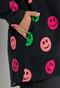 Czarna bluza z kolorowymi wzorami uśmiechniętych buziek w odcieniach różu i zieleni. Posiada przednią kieszeń i luźny krój. Wykonana z miękkiej bawełny.