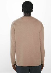 Langärmliges Hemd in einem sanften Tan-Farbton mit strukturierter Stoffqualität, ausgestattet mit einem runden Ausschnitt und einem lockeren Schnitt. Minimalistisches Design und klare Linien.