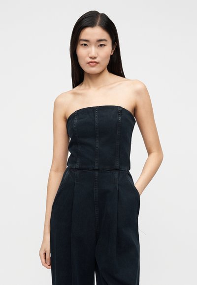 Mustast teksast rihmadeta kombinesoon vertikaalsete õmblusdetailidega, laiade sääreosade ja küljetaskutega. Matt tekstuur kerge läikega.