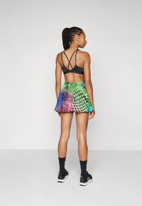 Sujetador deportivo negro con diseño de espalda entrecruzada, combinado con una falda corta de patrón colorido que presenta diseños geométricos en verde, azul, rosa y negro.