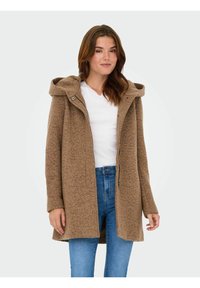 Bruine capuchonjas van textiel, met een vooraanlopende rits en zijzakken, gedragen over een wit shirt en blauwe jeans.