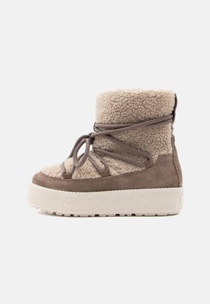 Bottines couleur beige et tan en polaire et daim avec un col duveteux, dotées de lacets et d'une semelle en caoutchouc texturé blanche.