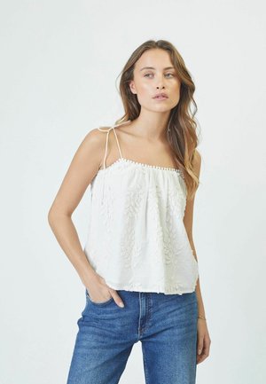 Weißes besticktes Trägertop mit dünnen verstellbaren Trägern und dekorativem Besatz. Kombiniert mit blauen Jeans im relaxten Schnitt.