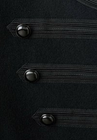 Czarna wełniana tkanina z trzema pionowymi pasami, z których każdy ozdobiony jest czarnym guzikiem, teksturowanym detalem oraz eleganckimi przeszyciami.