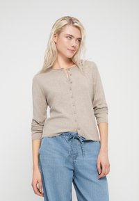 Light brown, knitted cardigan with a rounded neckline, full front button closure, and three-quarter sleeves, paired with loose blue denim pants.