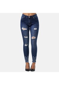 Jeans ajustados de denim oscuro, con múltiples desgastes y dobladillos deshilachados. Acentuados con costuras decorativas en los tobillos.