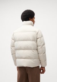 Light beige puffer jacket with a high collar, horizontal quilted design, and soft texture. The jacket features a relaxed, oversized fit.