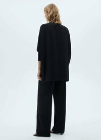 Maglietta nera in maglia oversize con vestibilità ampia, maniche a tre quarti e tessuto testurizzato, abbinata a pantaloni larghi neri coordinati.