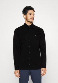 Schwarzes Langarmhemd mit Button-Down-Kragen, das ein tailliertes Design, eine glatte Textur und ein kleines, auf der Brust gesticktes Logo aufweist.
