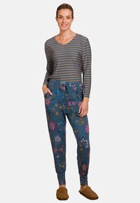 Gestreepte lange mouw top in donkerblauw, gecombineerd met joggers met een blauw bloemenpatroon; heeft zijzakken en een elastische tailleband. Zachte bruine slippers.