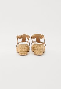Sandali platform tan con suole in giuta intrecciata, sottili cinghie alla caviglia e disegni ritagliati. Texture liscia con un tacco leggermente rialzato.