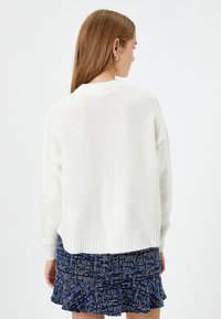 Weißer, gestrickter Pullover mit lockerer Passform und geripptem Saum, kombiniert mit einem dunkelblauen, strukturierten Minirock mit fransigem Rand.
