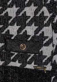 Czarny i szary materiał dzianinowy w wzór houndstooth z metalicznymi nićmi, z dodatkami w postaci guzika i zamka z detalami logo.