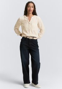 Lys gul stribet bluse med lange ærmer og to brystlommer, kombineret med mørkeblå vide jeans og hvide sneakers.
