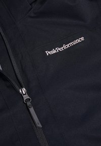 Giacca nera con logo PeakPerformance ricamato in filo bianco, con chiusura a zip e tessuto liscio e resistente.