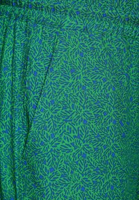 Grön tyg med ett bladmönster i mörkare blått, med en strukturerad yta och ett elastiskt midjeband. Inkluderar sidofickor.