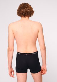 Boxer shorts neri in cotone con vita elasticizzata, dotati di un logo e dettagli rossi, visti da dietro. Tessuto liscio, design aderente.