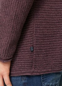 Sweter dzianinowy w ciemnym burgundzie, z fakturą w prążki, długimi rękawami oraz małą czarną metką przy dolnej krawędzi. Szczegóły widoczne na mankiecie.