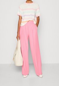 Camiseta de rayas en tela suave con colores pastel, combinada con pantalones de pierna ancha rosa de cintura alta, zapatos blancos de punta y un bolso ligero.