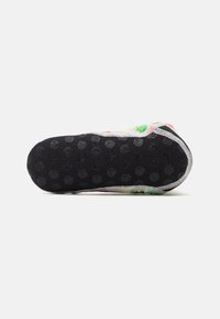 Sole di scarpa colorata con un fondo in gomma nera testurizzata caratterizzato da modelli a grip circolari e un bordo cucito bianco.