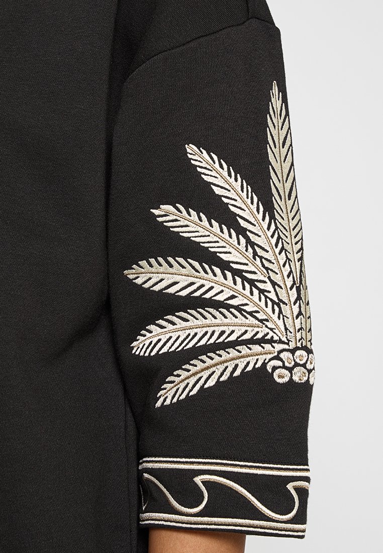 Sudadera negra con bordado de hojas de palma metálicas en dorado y plateado en la manga, con puños con diseño y textura suave.