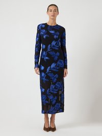 Svart klänning med långa ärmar, med blå blomsterbroderi. Genomskinlig textur, kroppsnära passform och längd till mitten av vadmuskeln. Bruna klackar.