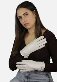 Guanti in pelle bianca con una texture liscia e dettagli cuciti, dotati di chiusura a cinturino. Indossati da una modella con un top nero.