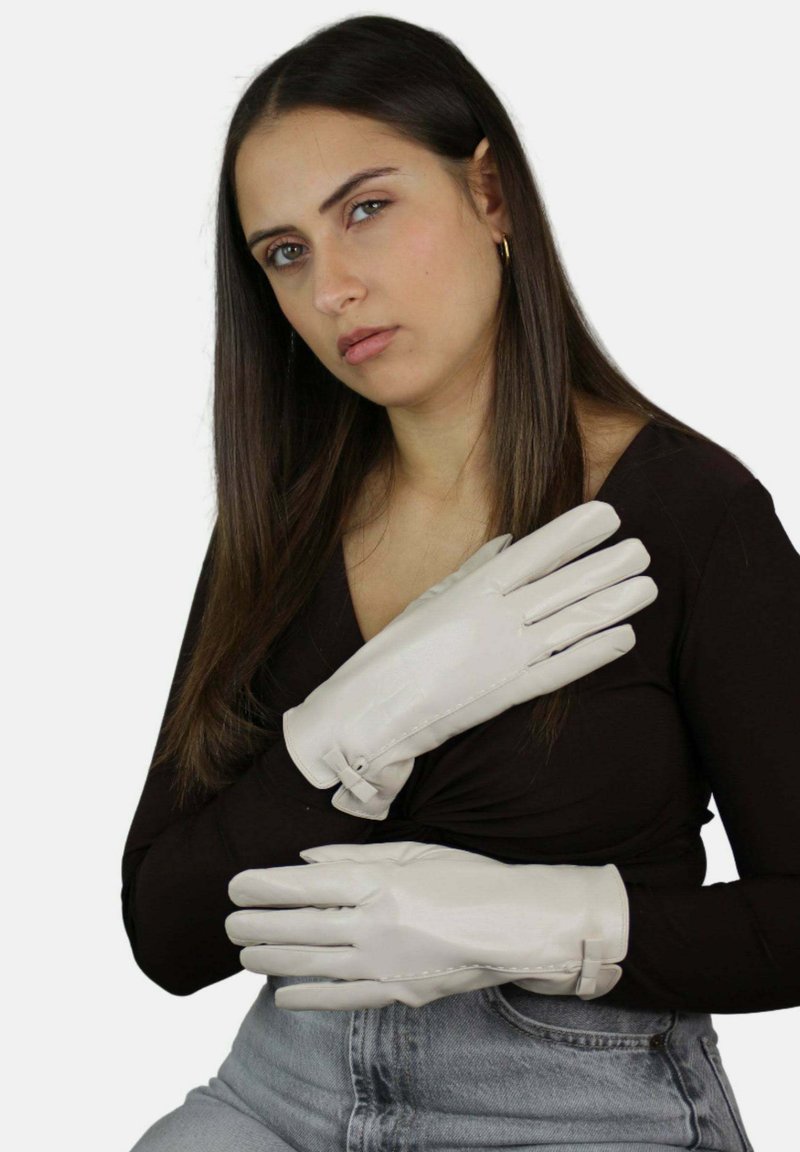 Guanti in pelle bianca con una texture liscia e dettagli cuciti, dotati di chiusura a cinturino. Indossati da una modella con un top nero.