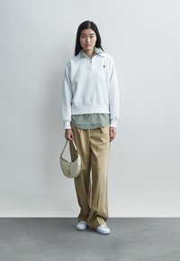 Weißes Sweatshirt über einem grünen, gestreiften Hemd mit Kragen, beige Schlaghosen, weiße Turnschuhe und eine kleine cremefarbene Handtasche. Minimalistisches Design.