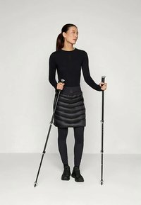 Μαύρος πουλόβερ, μαύρη θερμική φούστα και μαύρες κολάν. Κρατώντας μπαστούνια πεζοπορίας, φορώντας σκούρα παπούτσια, με λεία υφή σε όλη την επιφάνεια.