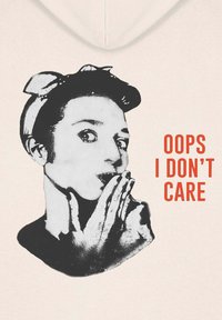 Mikina s kapucňou v svetlej béžovej farbe s čiernou grafikou osoby, ktorá si priložila prst na pery. Text znie "OOPS I DON'T CARE" tučným červeným písmom.